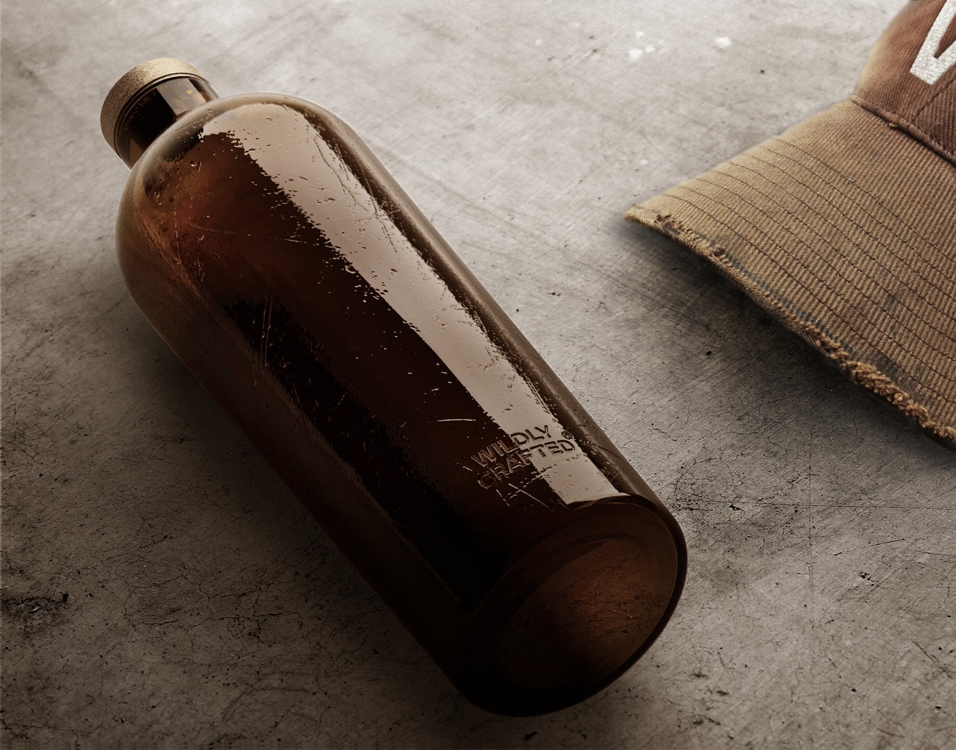 Estal Wildly Crafted Náladový obrázok: hnedá fľaša z kolekcie Wildly Crafted leží na sivom betónovom podklade, vedľa nej hnedá šiltovka
